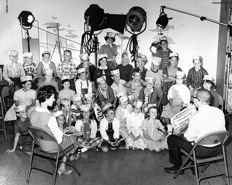 "Wide grins crease faces of young students as they sit in newspaper photographic studio with Mrs. Joelle Green, left, their teacher, and Valley Times Today staff writer Jerry Burns. Youngsters had just finished two-hour tour of paper in connection with National Newspaper Week." Order #00113556